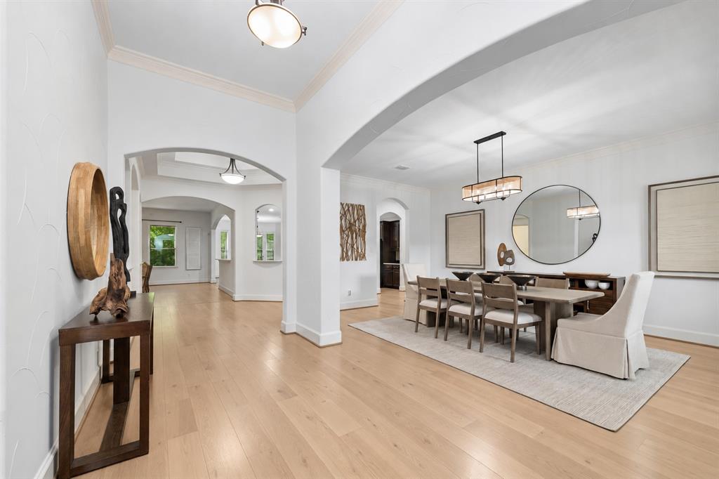 Light wood-finish flooring, arched doorways, crown molding, a rectangular chandelier, and recessed lighting