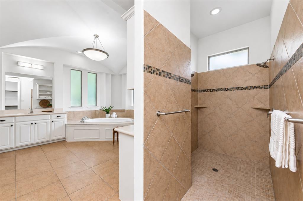 Spacious bathroom featuring a built-in soaking tub, dual vanity with undermount sinks, and a walk-in shower with tile surround and built-in shelving