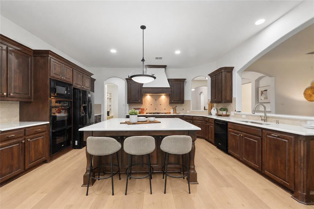 Spacious kitchen featuring an expansive center island with seating, dark wood cabinetry, light wood-finish flooring, and integrated black appliances