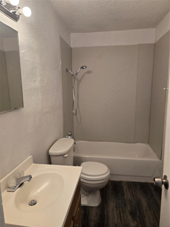 Bathroom featuring wood-finish flooring, a white vanity with an integrated sink, a built-in bathtub, and a shower with a chrome fixture