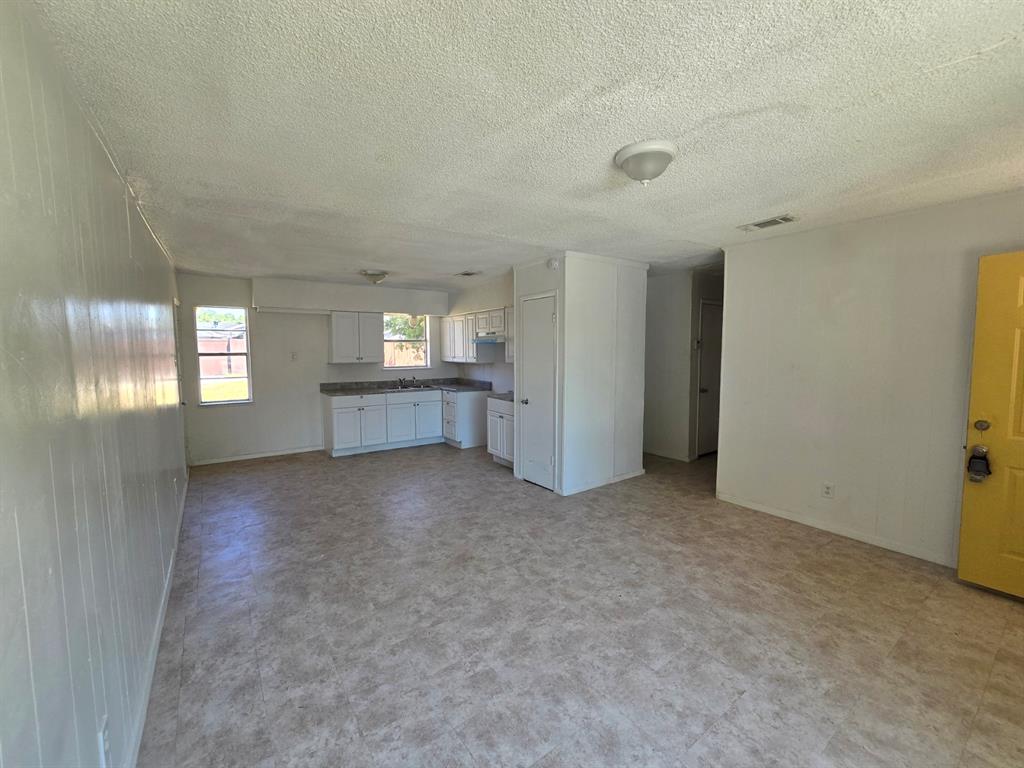 Open-concept living area with vinyl plank flooring, a kitchen featuring white cabinetry and laminate countertops, and multiple windows providing natural light
