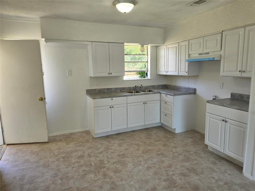 Kitchen featuring white cabinetry, gray speckled countertops, a double basin stainless steel sink, and light-toned linoleum flooring