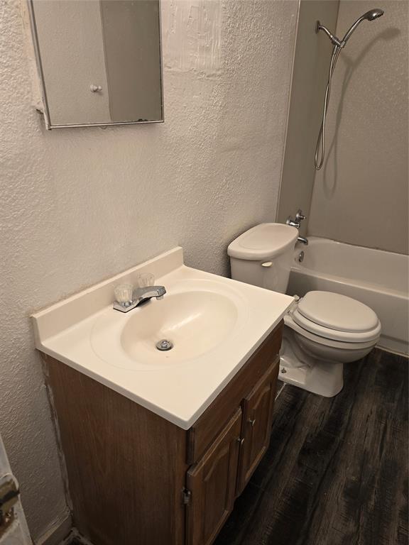 Wood-finish flooring, vanity with integrated sink, chrome faucet, toilet, and bathtub with shower fixture