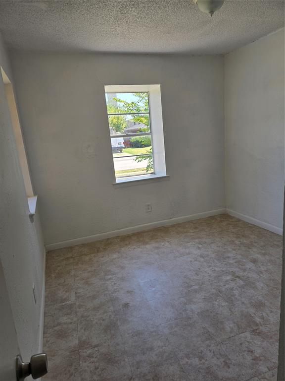 Neutral wall paint, textured ceiling, tile-look flooring, and a single window