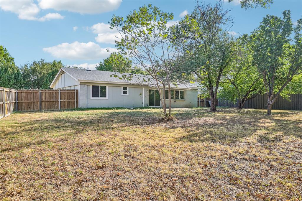 Expansive backyard featuring a wood fence, mature trees, and a slider door entry