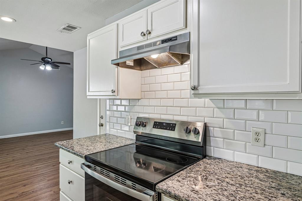 White subway tile backsplash, stainless steel electric range, granite-finish countertops, white cabinetry, wood-finish flooring