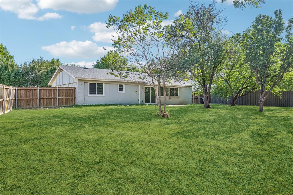 Expansive backyard featuring a lush lawn, mature trees, wood privacy fencing, and a sliding glass door