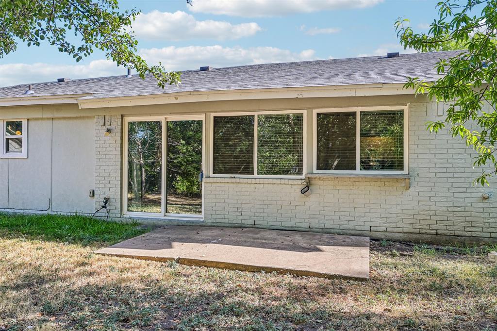Sliding glass door, multiple large windows, exterior brick detail, concrete patio, and a shingled roof