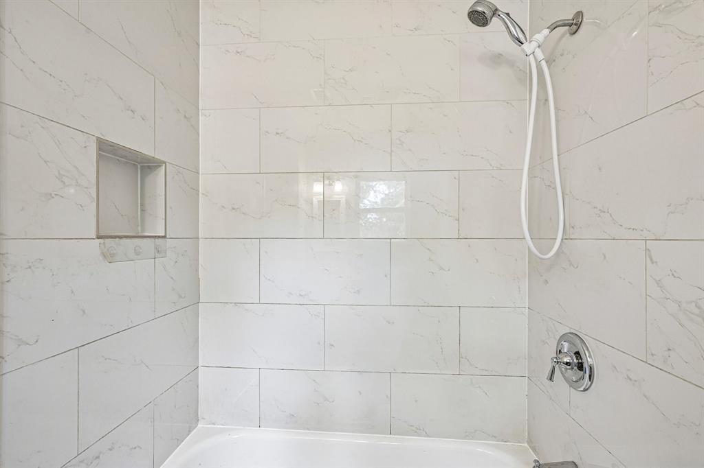 Bathtub with a chrome shower head and faucet, white subway tile surround, and a recessed shower niche