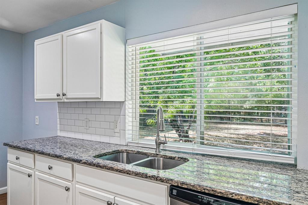 White shaker-style upper and lower cabinetry, speckled stone countertops, undermount double-basin sink with a pull-down faucet, and white subway tile backsplash