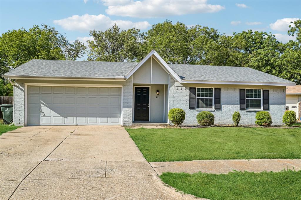 Brick exterior with a gabled roofline, attached garage, well-maintained lawn, and mature trees