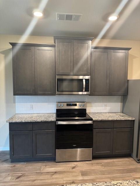 Kitchen featuring dark gray cabinetry, stainless steel appliances, granite countertops, white subway tile backsplash, and wood-finish flooring Kitchen featuring dark gray cabinetry, stainless steel appliances, granite countertops, white subway tile backsplash, and wood-finish flooring