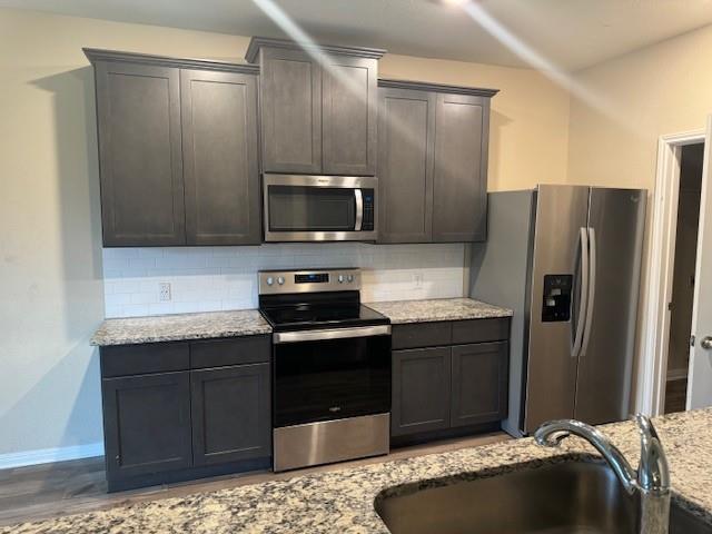 Kitchen featuring dark wood-finish cabinetry, stainless steel appliances, speckled stone countertops, and a subway tile backsplash Kitchen featuring dark wood-finish cabinetry, stainless steel appliances, speckled stone countertops, and a subway tile backsplash