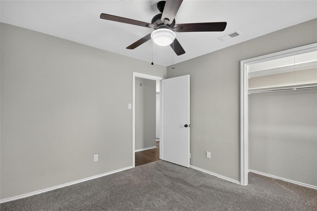 Plush grey carpet flooring, light grey painted walls, ceiling fan with integrated lighting, and a closet with a built-in hanging rod