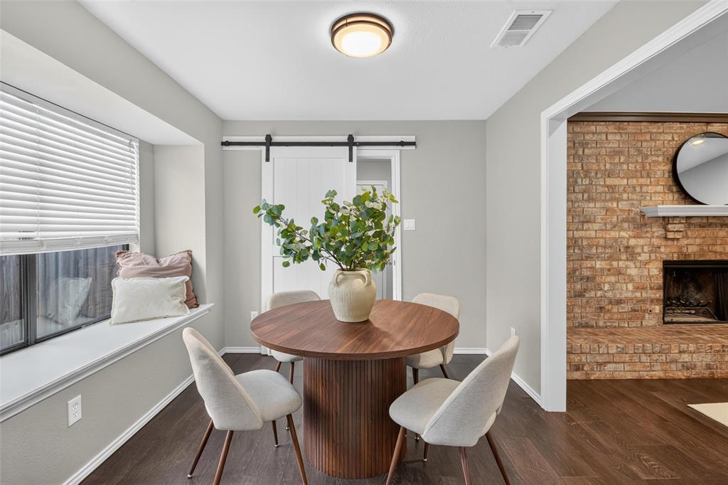 Recessed window seat, wood-finish flooring, white barn door, brick fireplace, and built-in lighting