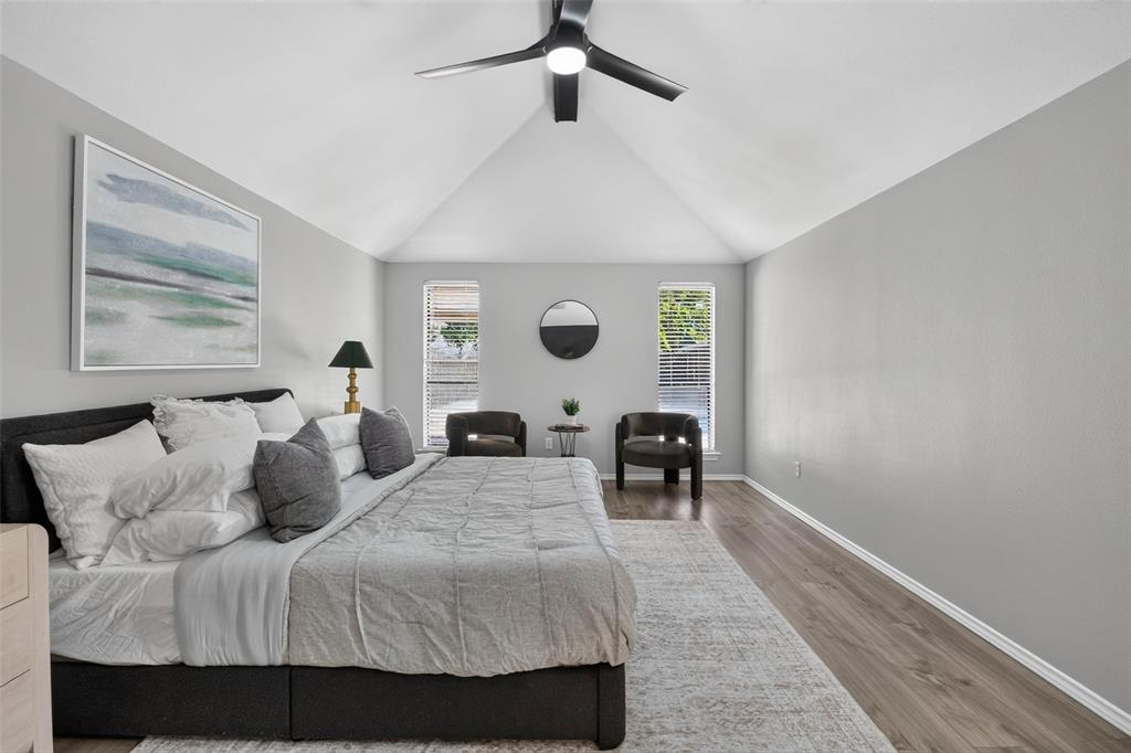 Vaulted ceiling, wood-finish flooring, two windows with blinds, and a ceiling fan with integrated lighting