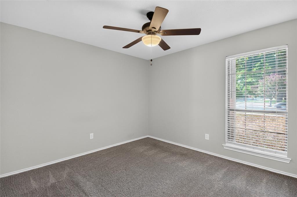 Bright corner bedroom with neutral wall finishes, plush carpeting, ceiling fan with integrated light fixture, and large window with plantation shutters providing natural light and privacy