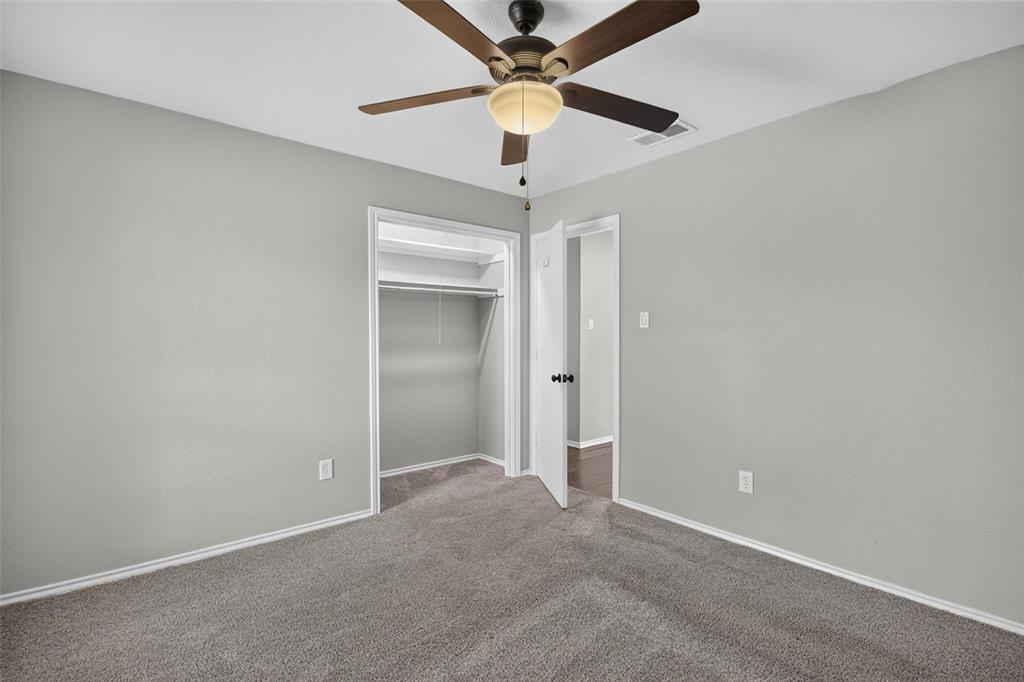 Neutral tone walls, ceiling fan with integrated lighting, gray carpeting, and a built-in closet with shelving
