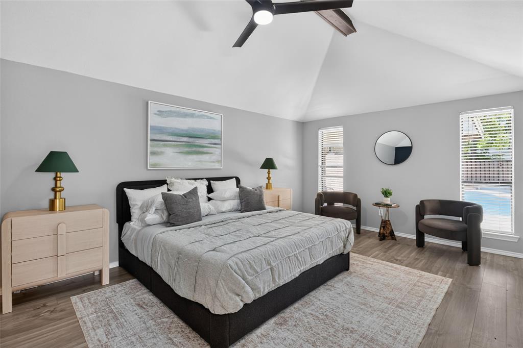 Vaulted ceiling with exposed wood beam, wood-finish flooring, recessed windows with horizontal blinds, and a ceiling fan with integrated lighting