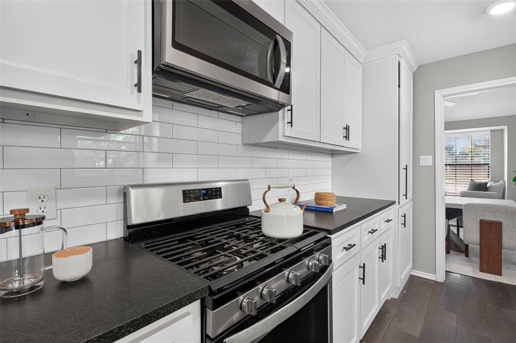 White shaker cabinetry, dark countertops, white subway tile backsplash, stainless steel microwave, and wood-finish flooring