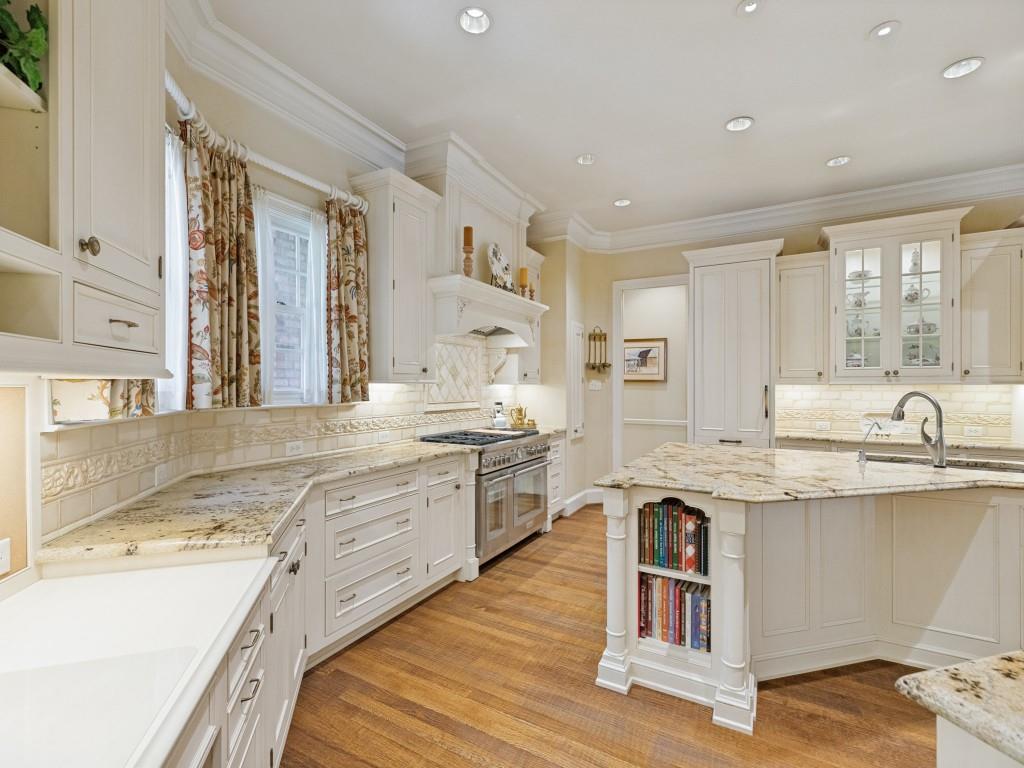 Custom cabinetry with glass-front accents, granite countertops, tile backsplash, wood-finish flooring, and recessed lighting
