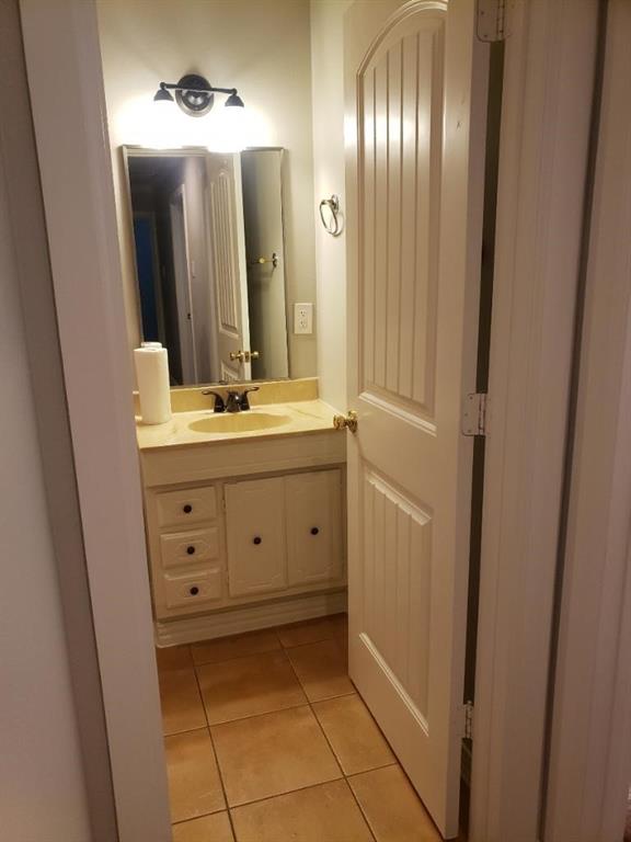 Vanity with a single basin, wall-mounted light fixture, and tile flooring