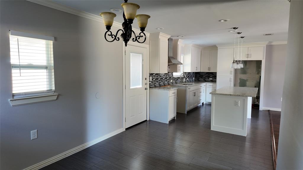 Open-concept kitchen and dining area featuring wood-finish flooring, white cabinetry, granite countertops, and a mosaic tile backsplash Open-concept kitchen and dining area featuring wood-finish flooring, white cabinetry, granite countertops, and a mosaic tile backsplash