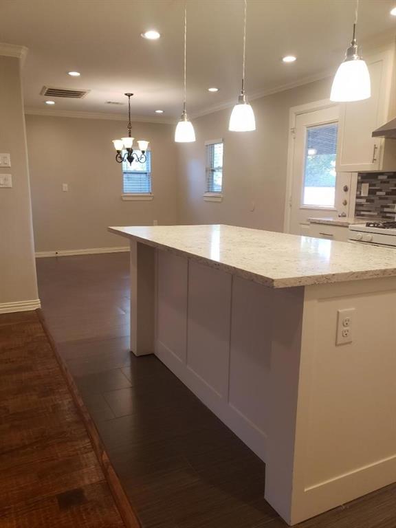 Modern kitchen featuring a substantial island with a light stone countertop, pendant lighting with frosted glass shades, recessed ceiling lights, and stainless steel appliances