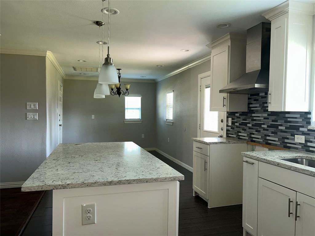 Kitchen featuring white cabinetry, stone countertops, dark wood-finish flooring, a mosaic tile backsplash, and stainless steel range hood Kitchen featuring white cabinetry, stone countertops, dark wood-finish flooring, a mosaic tile backsplash, and stainless steel range hood