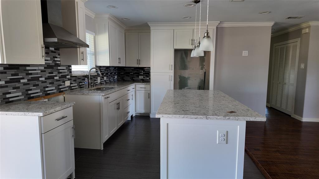 Kitchen featuring white cabinetry, light-toned countertops, a mosaic tile backsplash, a stainless steel range hood, and dark wood-finish flooring Kitchen featuring white cabinetry, light-toned countertops, a mosaic tile backsplash, a stainless steel range hood, and dark wood-finish flooring