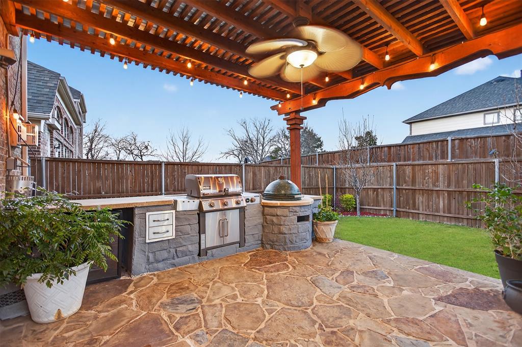 Expansive stone patio featuring a built-in outdoor kitchen with grill, wood pergola, and string lighting
