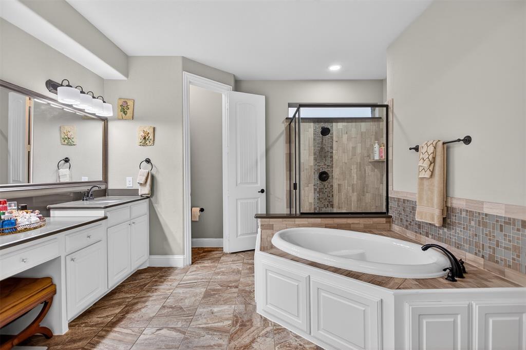 Spacious bathroom featuring a built-in soaking tub, glass-enclosed shower with tile surround, dual vanity with white cabinetry, and wood-finish flooring
