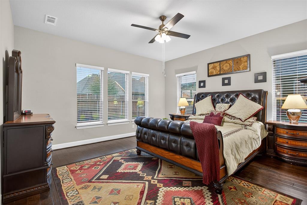Dark wood-finish flooring, ceiling fan with integrated lighting, three windows with blinds, and light gray wall paint