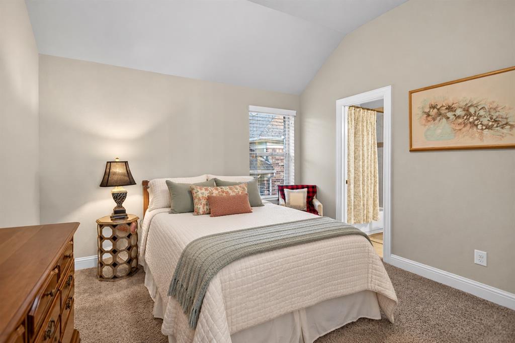 Vaulted ceiling, neutral wall tones, window with horizontal blinds, carpeted flooring, and a doorway leading to an adjoining space
