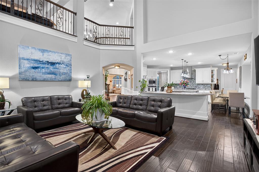 Two-story living area with dark wood-finish flooring, wrought iron railings, and a kitchen featuring white cabinetry, pendant lighting, and a tile backsplash Two-story living area with dark wood-finish flooring, wrought iron railings, and a kitchen featuring white cabinetry, pendant lighting, and a tile backsplash