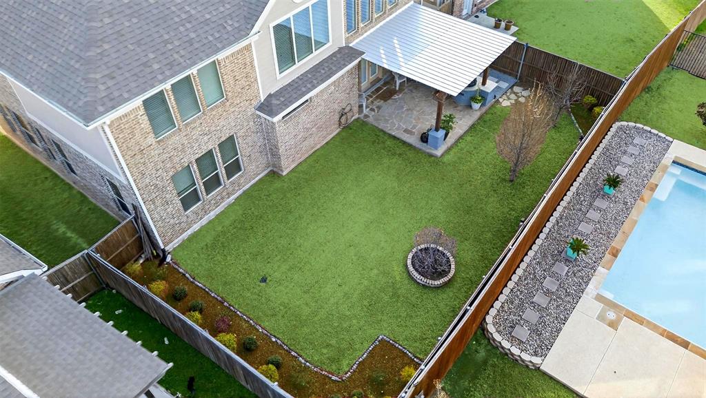 Expansive backyard featuring a swimming pool with concrete surround, artificial turf lawn, built-in fire pit, and a covered patio with stone pavers