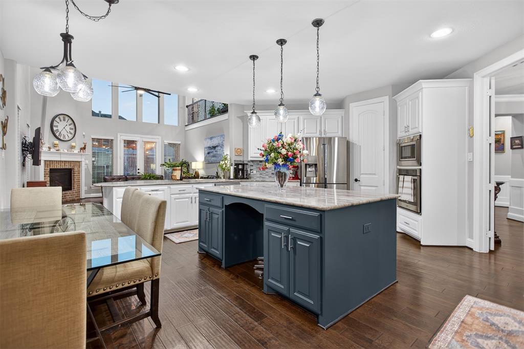 Open-concept kitchen with a two-story ceiling, a large kitchen island, stainless steel appliances, and wood-finish flooring Open-concept kitchen with a two-story ceiling, a large kitchen island, stainless steel appliances, and wood-finish flooring