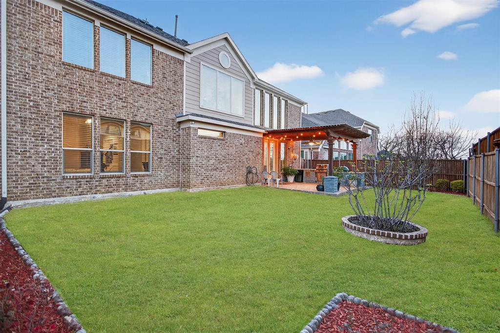 Brick exterior with multiple windows, covered patio with string lighting, paved patio area, and a fenced backyard