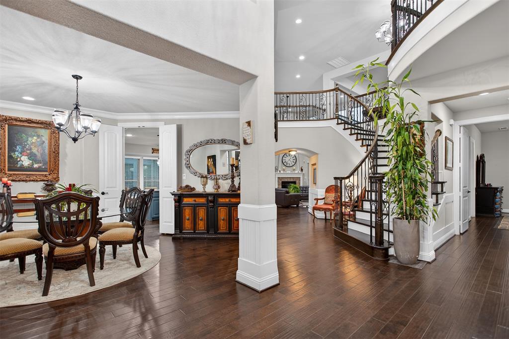 Dark wood-finish flooring, a grand curved staircase with wrought iron balusters, a formal dining area with chandelier, and tall ceilings Dark wood-finish flooring, a grand curved staircase with wrought iron balusters, a formal dining area with chandelier, and tall ceilings