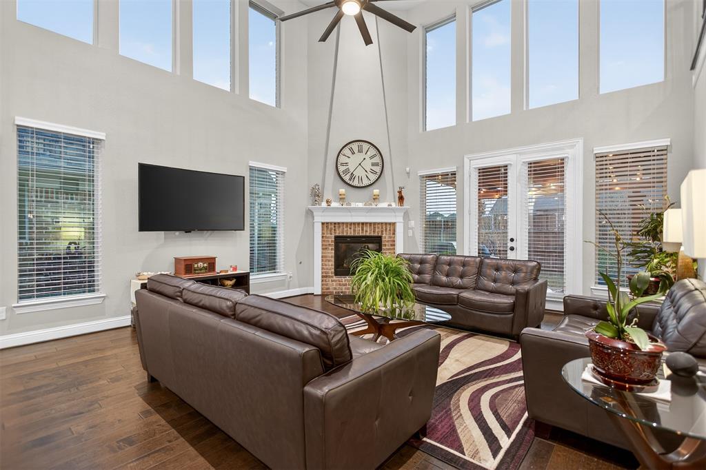 Wood-finish flooring, high ceilings with clerestory windows, ceiling fan, brick fireplace with mantel, and double glass doors