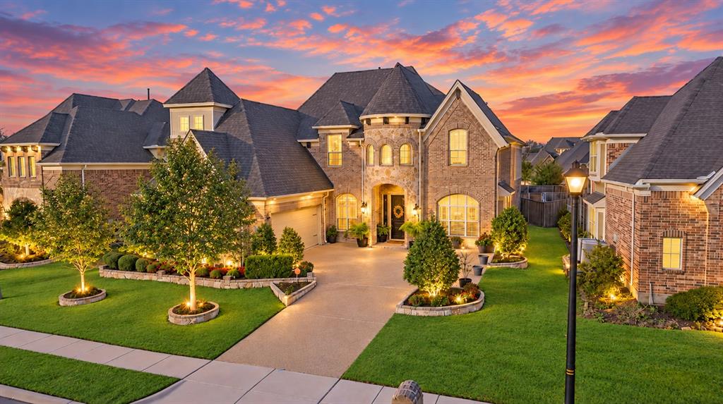 Brick exterior with stone accents, turret detail, gabled rooflines, a concrete driveway, and landscaped front yard with integrated lighting Brick exterior with stone accents, turret detail, gabled rooflines, a concrete driveway, and landscaped front yard with integrated lighting