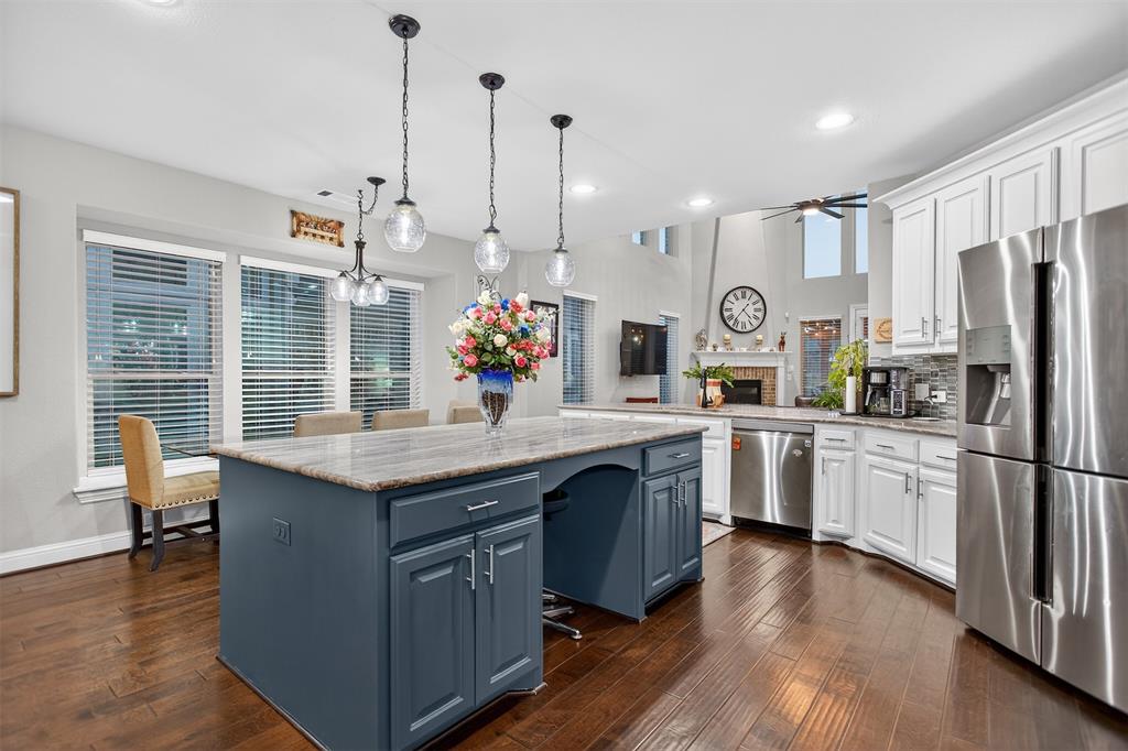 Wood-finish flooring throughout, central island with seating, stainless steel appliances, white cabinetry, and a tile backsplash Wood-finish flooring throughout, central island with seating, stainless steel appliances, white cabinetry, and a tile backsplash