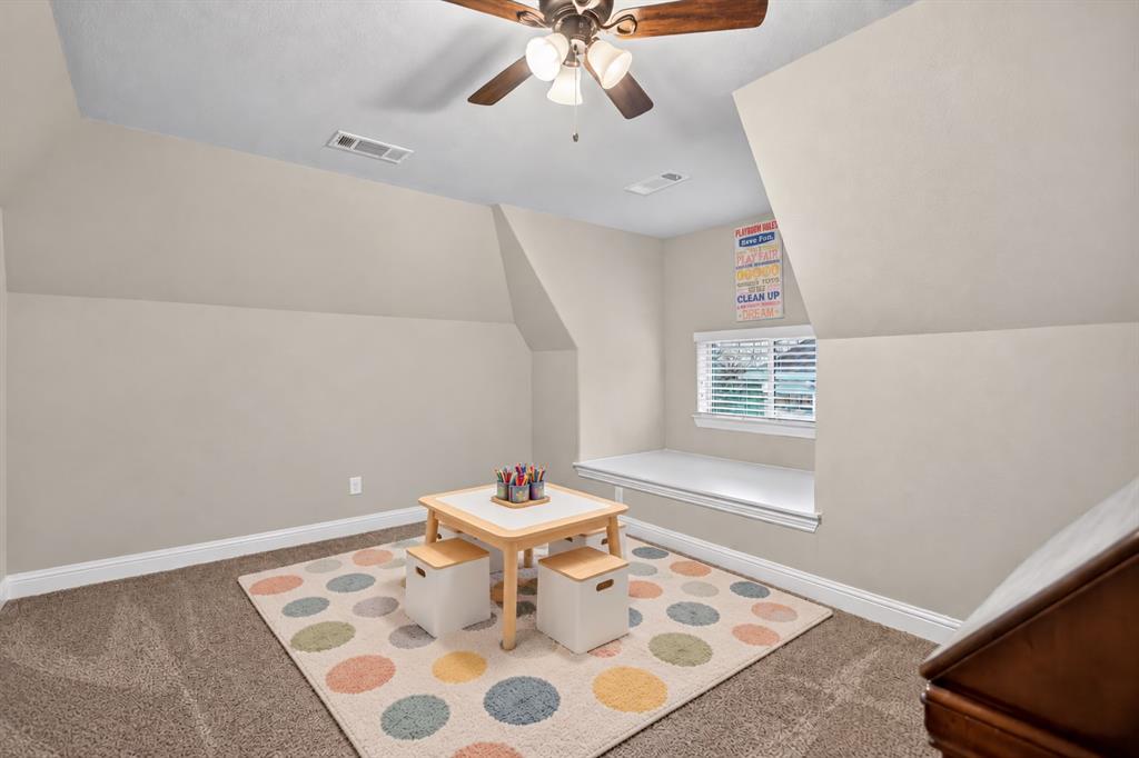 Carpeted flooring, sloped ceilings, ceiling fan with integrated lighting, window with blinds, and a built-in window seat