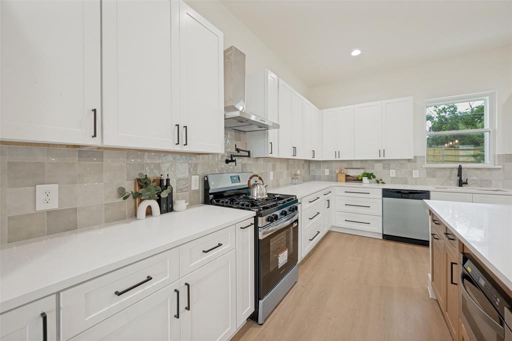 Contemporary kitchen featuring white cabinetry, light-toned countertops, a stainless steel range with a ventilation hood, and light-colored tile backsplash