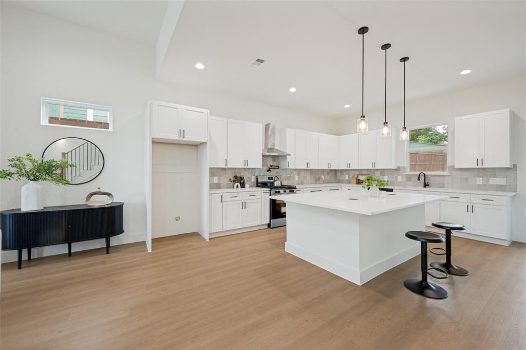 Spacious kitchen featuring an expansive island with a light-toned countertop, white cabinetry with dark hardware, and a tile backsplash