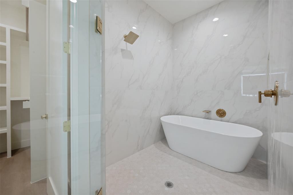 Freestanding soaking tub, large format tile shower surround, and gold-finish fixtures