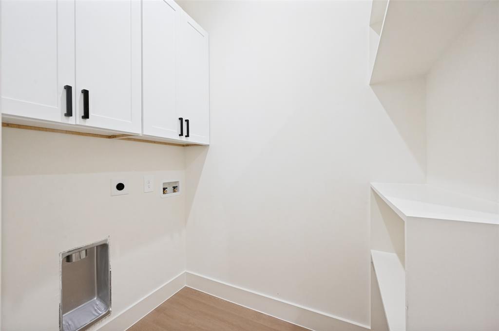 White cabinetry with black hardware, built-in shelving, light wood-finish flooring, and white walls