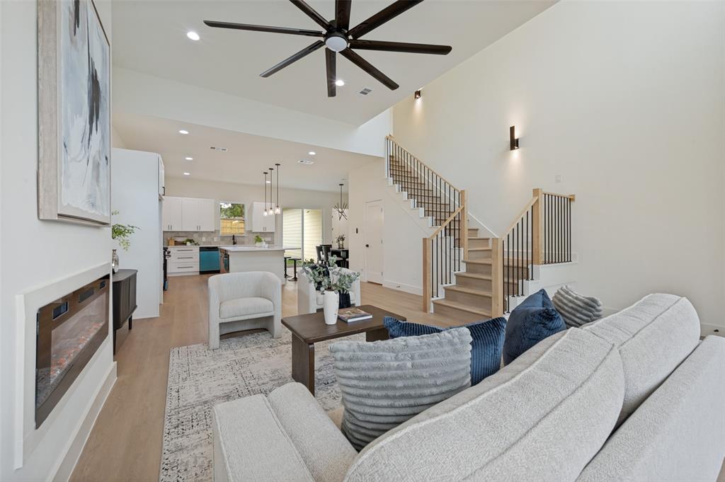 Spacious living area featuring a modern fireplace, high vaulted ceilings, wood-finish flooring, a contemporary ceiling fan, and a staircase with wood handrails and black iron balusters