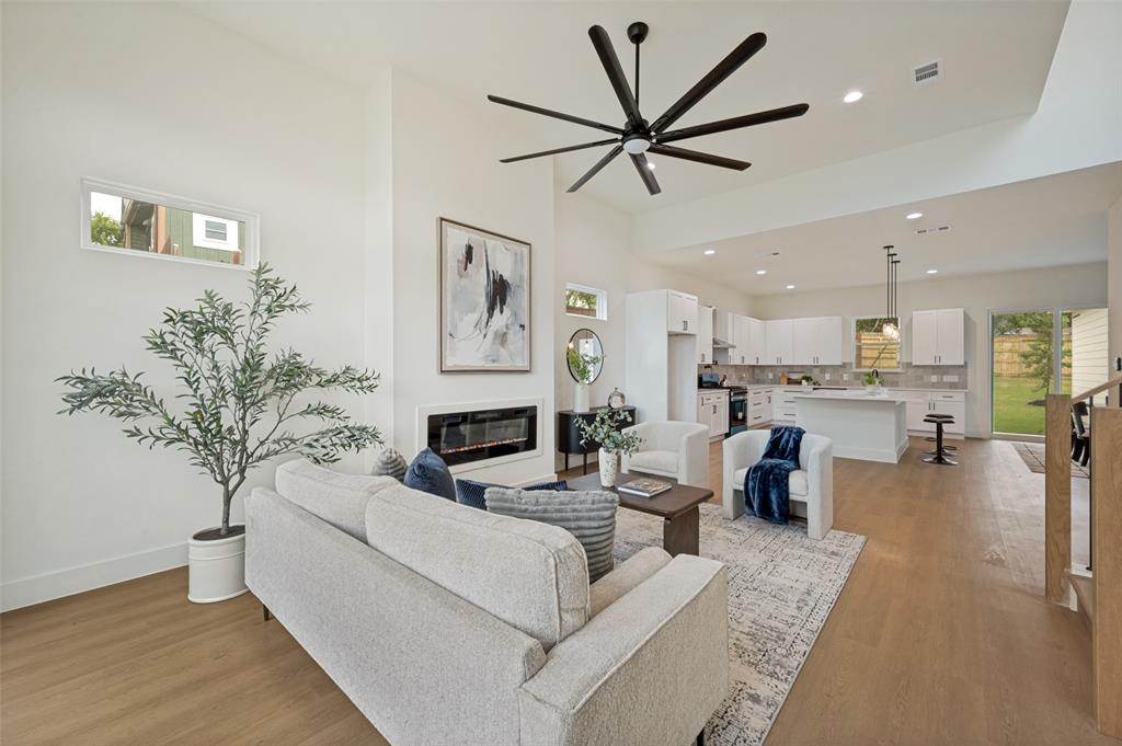 Vaulted ceilings, wood-finish flooring, a modern linear fireplace, and a kitchen featuring white cabinetry with a central island and pendant lighting