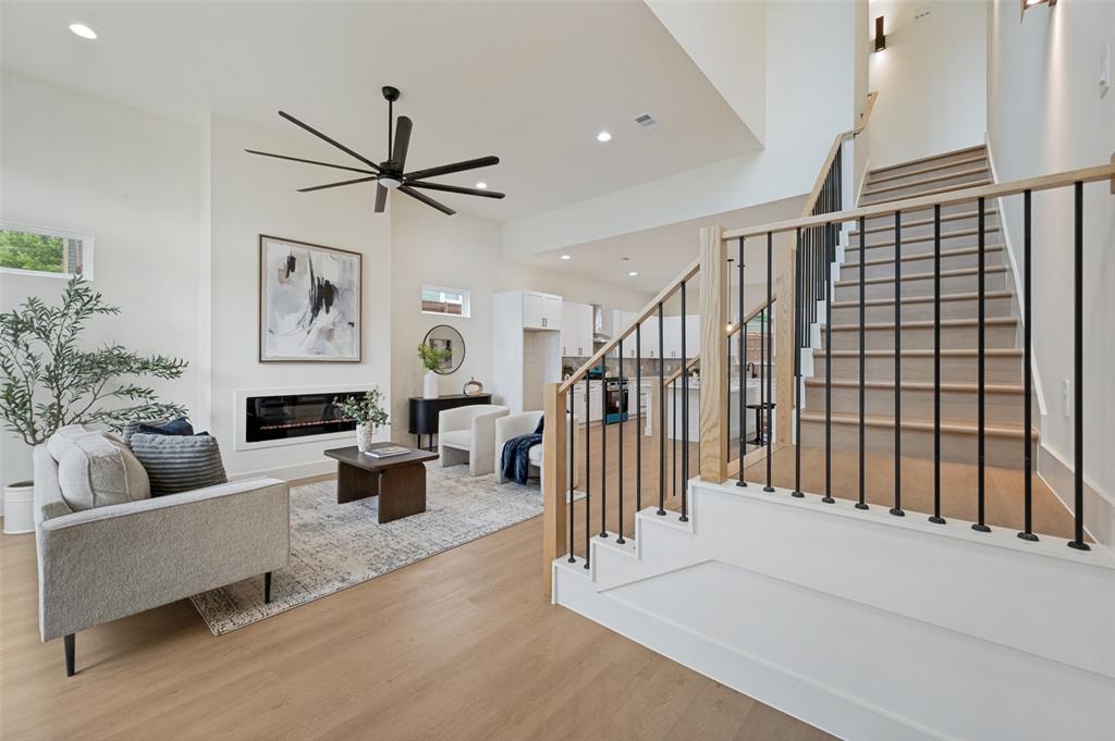 Vaulted ceiling, built-in linear fireplace, wood-finish flooring, staircase with black metal balusters and wood handrail, and recessed lighting